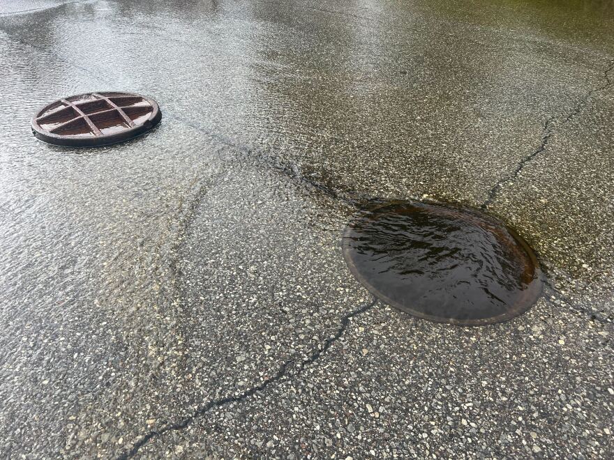 An open manhole cover seeping sewage onto a street.