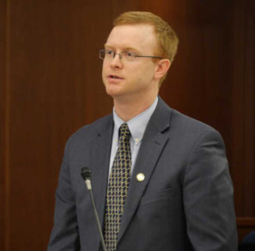 A man with red hair and glasses in a suit speaking in front of a microphone