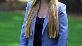 Portrait of Rebecca Scofield. She wears a periwinkle suit and black top with long blonde hair.