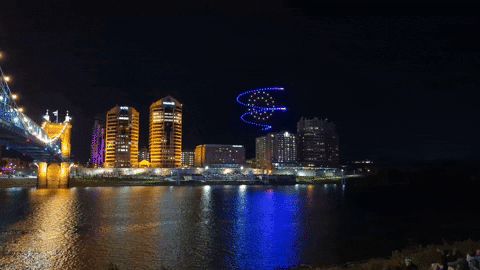 Illuminated drones form a blue spiral above the Ohio River, with Covington in the background.