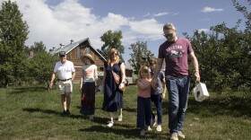 Six members of a family dressed in summer clothing walk through the grass with trees and a barn in the background. 