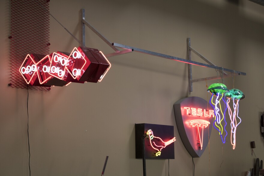 Neon signs of dice, a bird, the Tesla logo and jellyfish hang in Ken Hines' studio. 