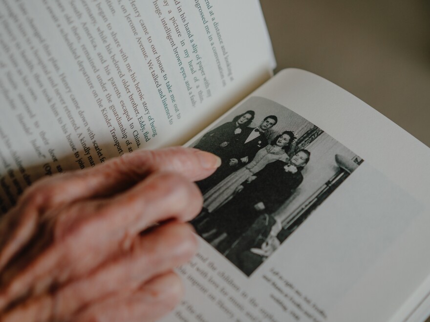 Estelle Laughlin points to a photo of (left to right) herself; her brother-in-law Sol; her sister, Fredka; and her mother at Fredka and Sol's wedding in 1948. The book she's holding is her memoir <em>Transcending Darkness: A Girl's Journey Out of the Holocaust.</em>