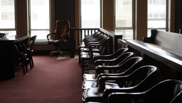 A row of chairs extends toward a back wall with tall windows that let the sunshine into a courtroom