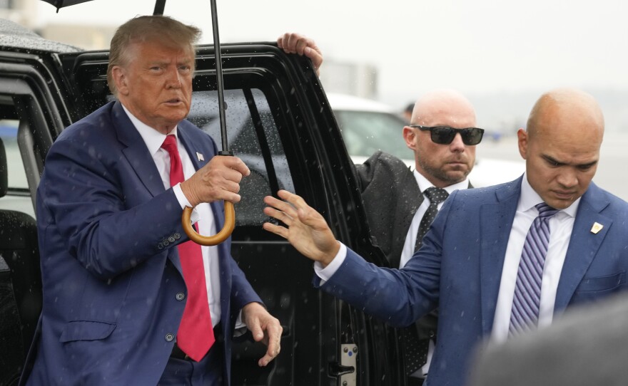 Former President Donald Trump is handed an umbrella by aide Walt Nauta as Trump arrives before boarding his plane at Ronald Reagan Washington National Airport, Thursday, Aug. 3, 2023, in Arlington, Va., after facing a judge on federal conspiracy charges. (AP Photo/Alex Brandon)