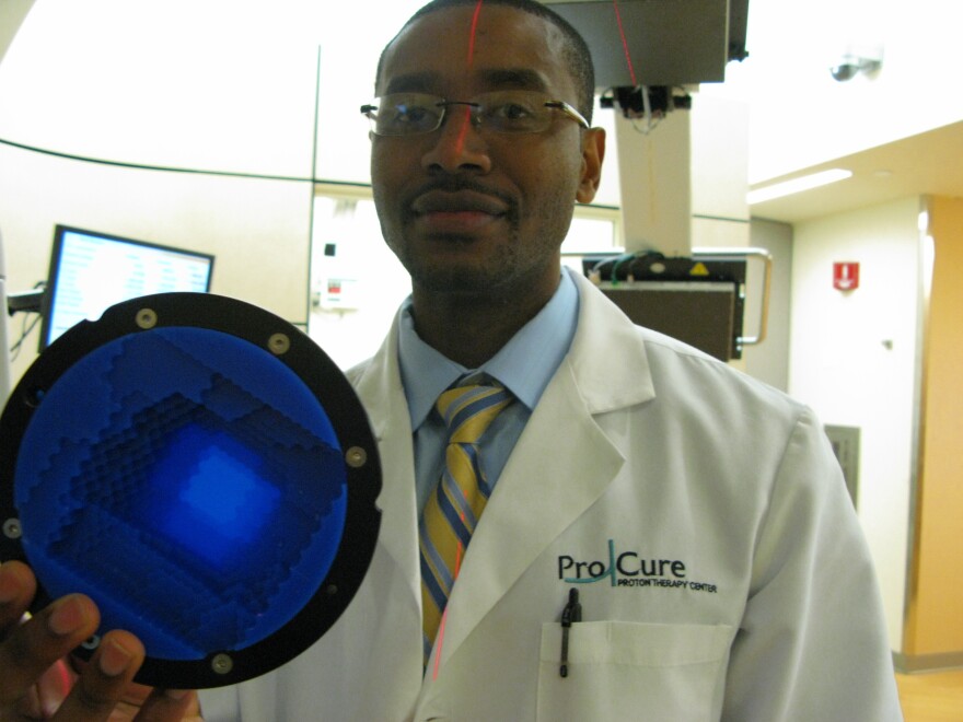 Radiation therapist Jean Etienne holds a range compensator, which shapes the depth to which the proton beam enters a patient's body to target a tumor.