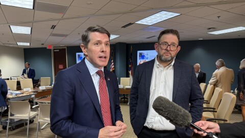 State Treasurer Brad Briner is standing next to Tom Friedman, executive administrator of the N.C. State Health Plan. Someone is holding a large microphone in front of them.