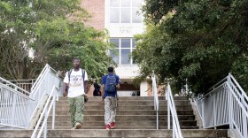 Two students walk down a long staircase. In back of them is a brick, campus building