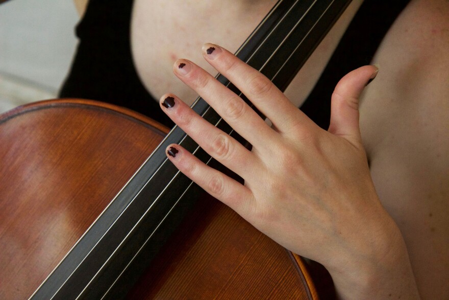 A woman's hand on the strings of a cello. 