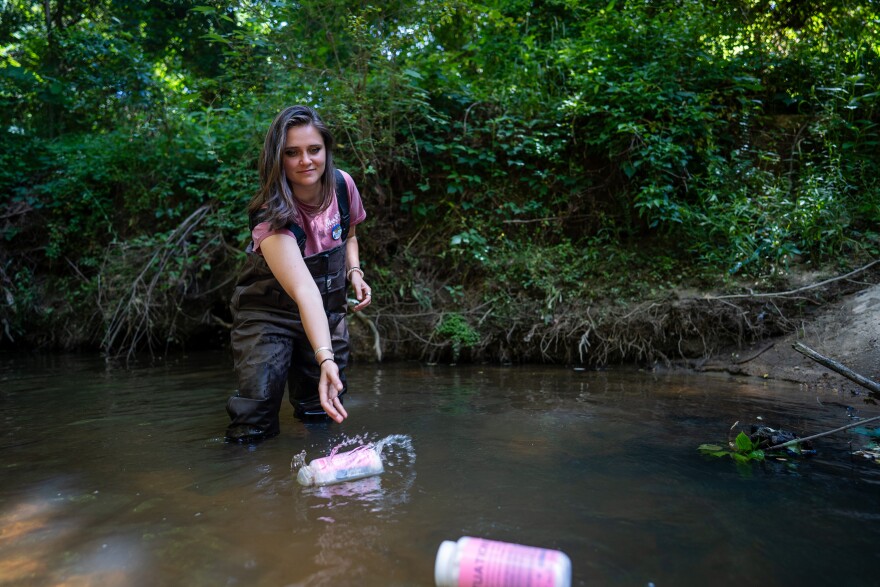A young woman throws plastic bottles into a creek