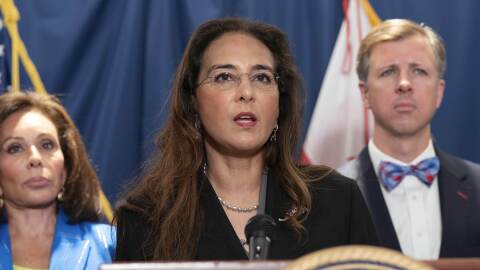 A woman in a jacket speaks at a podium.