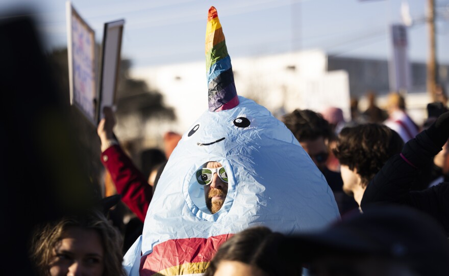 A man in a narwhal costume stands in a crowd at a rally. 