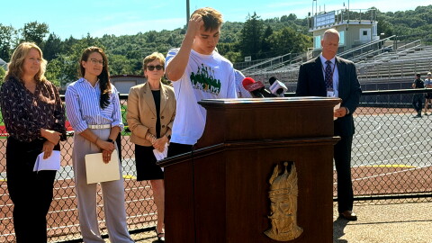 Ryan Dueker, an East Lyme High School lacrosse player and student ambassador at LAX2LIVE, a program to prevent youth suicide, spoke of the stressors that student athletes face on September 8, 2026.. He is flanked by state mental health officials. Behind him in a brown jacket is Ann Dagle, co-founder of the Brian Dagle Foundation and mother of Brian, a former student at the high school, who died by suicide when in college. The foundation runs the LAX2LIVE initiative.