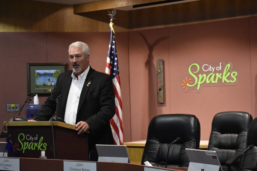 Ed Lawson stands at a podium that says “City of Sparks.” Behind him there is an American flag and another sign that reads, “City of Sparks.”