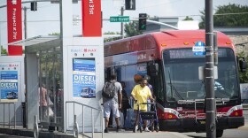 Exterior photo of a red transit bus stopped at a bus stop labeled "Prospect at 31st." People can be seen getting off the bus while others are waiting to get on.