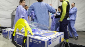 A medical face shield rests on boxes of gloves as nurses at Harborview Medical Center in Seattle hold a pre-shift meeting in a triage tent.