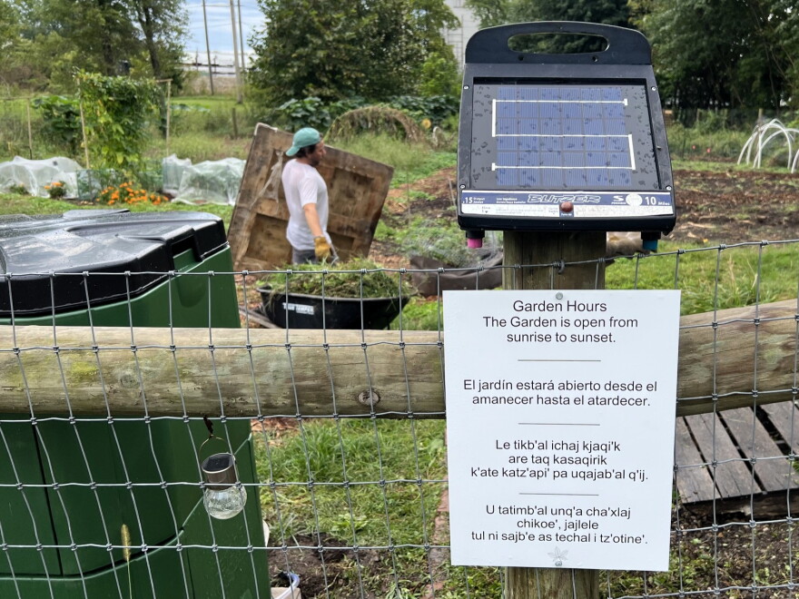 A sign posted to a fence announces the community garden hours in four languages.
