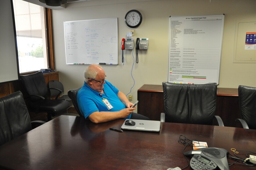 An employee sits in a crisis communications center for Saint Louis University Hospital. The red phone acts as a backup communication system, and the white boards track hospital resources in an emergency. 