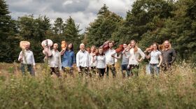 Eleven members of ACRONYM stand outside in a field on an early fall day. They're dressed casually and they all hold their instrument over their right shoulder -- even the cellists and viola de gamba players.