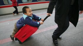 A boy hitches a ride on a suitcase as he waits to board a train at Beijing West Railway Station during the peak of travel for the Chunyun Spring Festival, in February 2007.