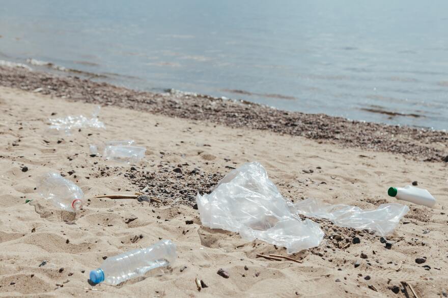 Plastic bottles and plastic film sits on sand near water