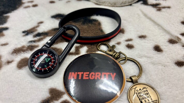 Mementos given to participants after each lesson. Integrity button, black bracelet with red stripe, a keychain encouraging teamwork and a compass. 
