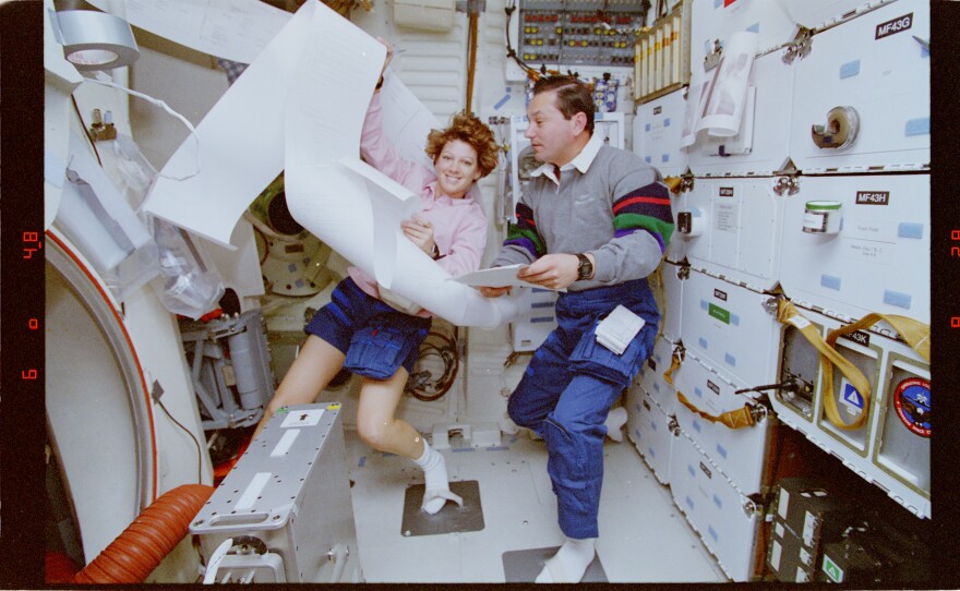 Pilot Eileen Collins and Mission Specialist Vladimir Titov posing with papers from the Thermal Impulse Printer System (TIPS) on the Space Shuttle Discovery's middeck during STS-63.