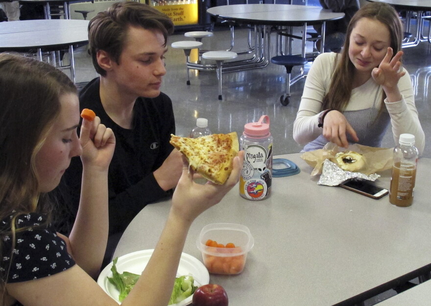 In this Friday, April 5, 2019 photo, Burlington High School student Emma McCobb, left, holds a piece of pizza while eating with classmates in the school cafeteria in Burlington, Vt.