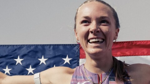 A young woman with a ponytail and sparkles on her face smiles as she holds an American flag out behind her.