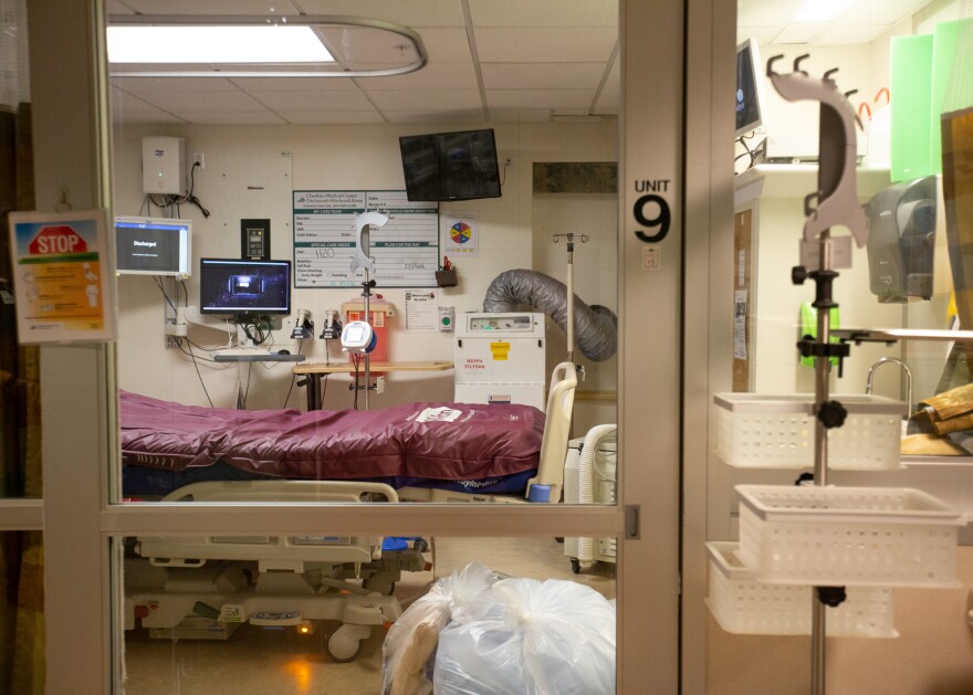 A photo of ICU unit 9. A gurney is inside, with a computer and other screens. A sign outside the glass door and windows says "Stop."