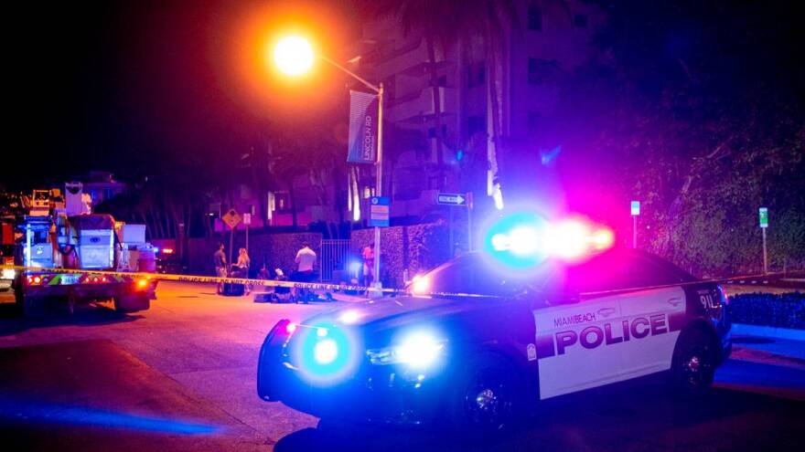 A Miami Beach police car and a fire truck sit behind crime tape with a siren light