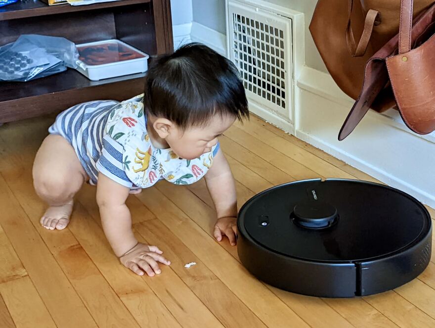  A toddler interacts with the family Roomba vacuum. 