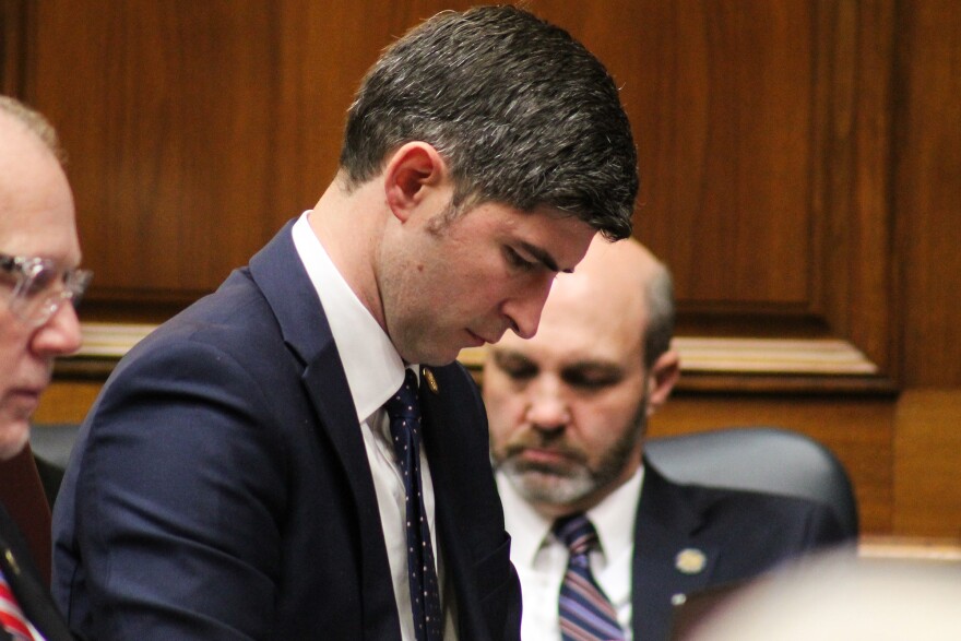 A man in a suit with short brown hair looks toward the floor in the House chamber.