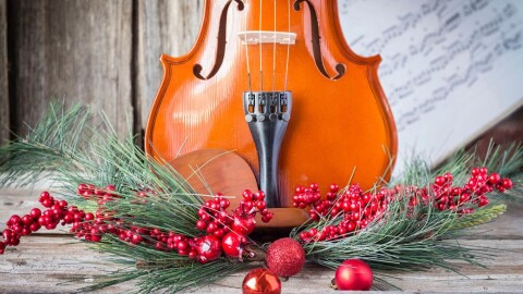 a violin resting upright on a swag of evergreen, holly berries and round, red Christmas tree ornaments