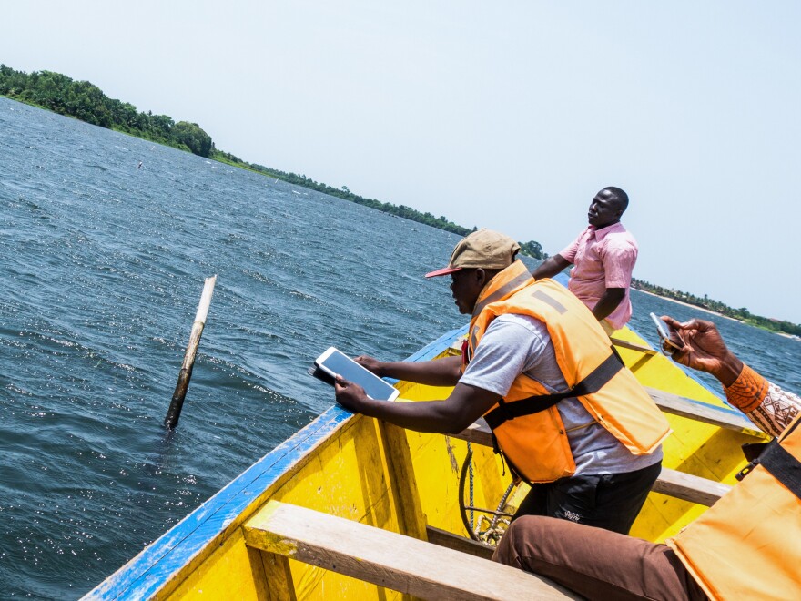 Samuel-Richard Bogobley holds a GPS-enabled tablet to capture the location of one corner of an underwater clam "farm" belonging to Kofi Amatey, in pink, in Ghana's Volta River estuary.