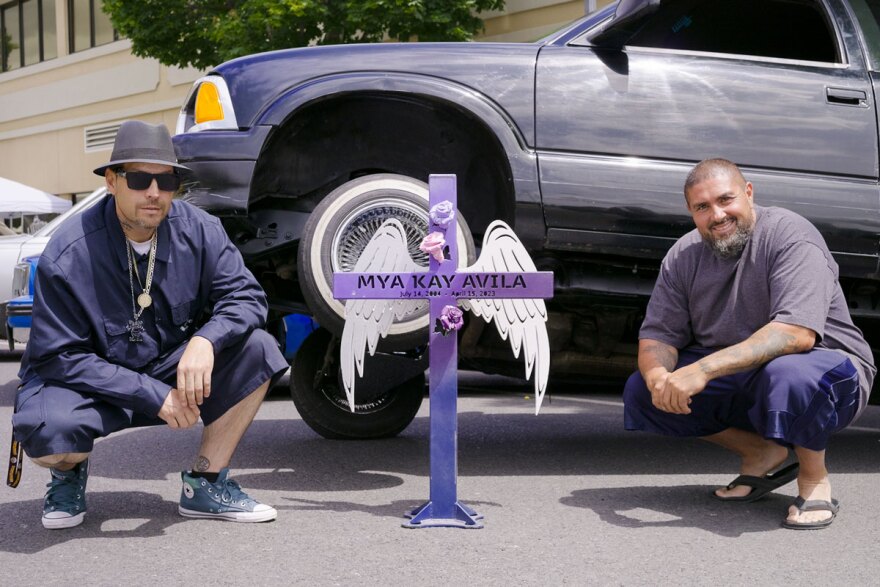 Car club president Jason Pastor-O’Neel (left) and car club vice president Cris Avila (Right) kneeling in front of the memorial lowrider truck dedicated to Mya Kay Avila.
