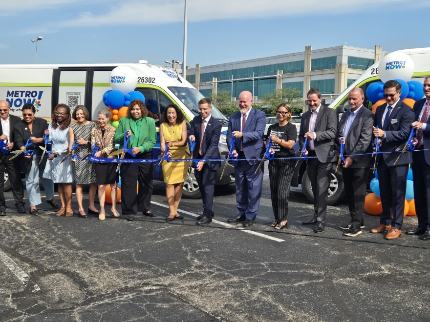 A group of people in dress clothes cut a ribbon in front of two transit vans