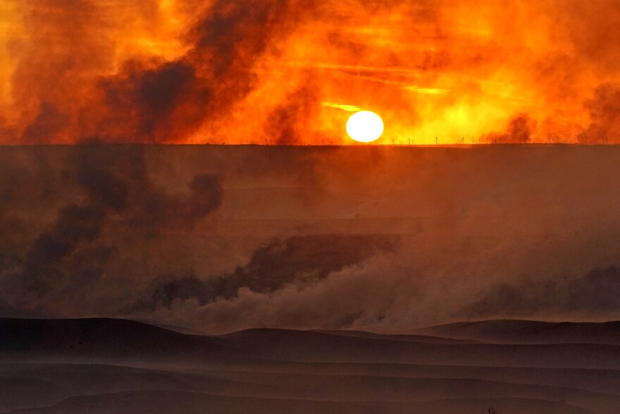 The setting sun is shrouded in smoke from a fire that burned and stretched across Ellis, Russell, Osborne and Rooks counties Thursday, Dec. 16, 2021, near Natoma, Kan. Firefighters and emergency responders are battling fires spreading across parts of central and western Kansas after a powerful storm blew through the state. 