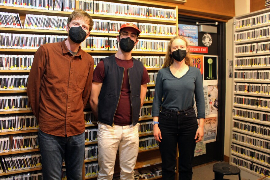 Two men and a woman standing in a radio studio wearing face masks