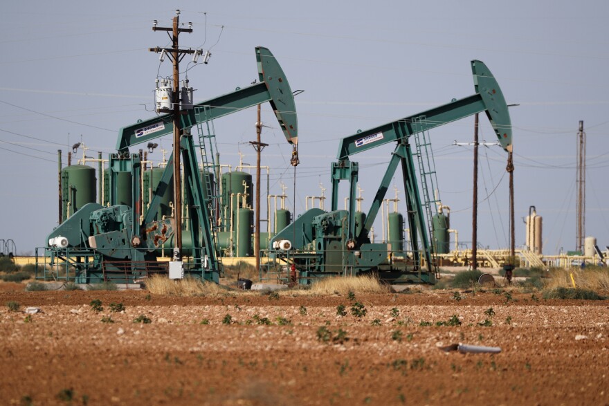 A pump jack operating in an oil field in a desert-like terrain.