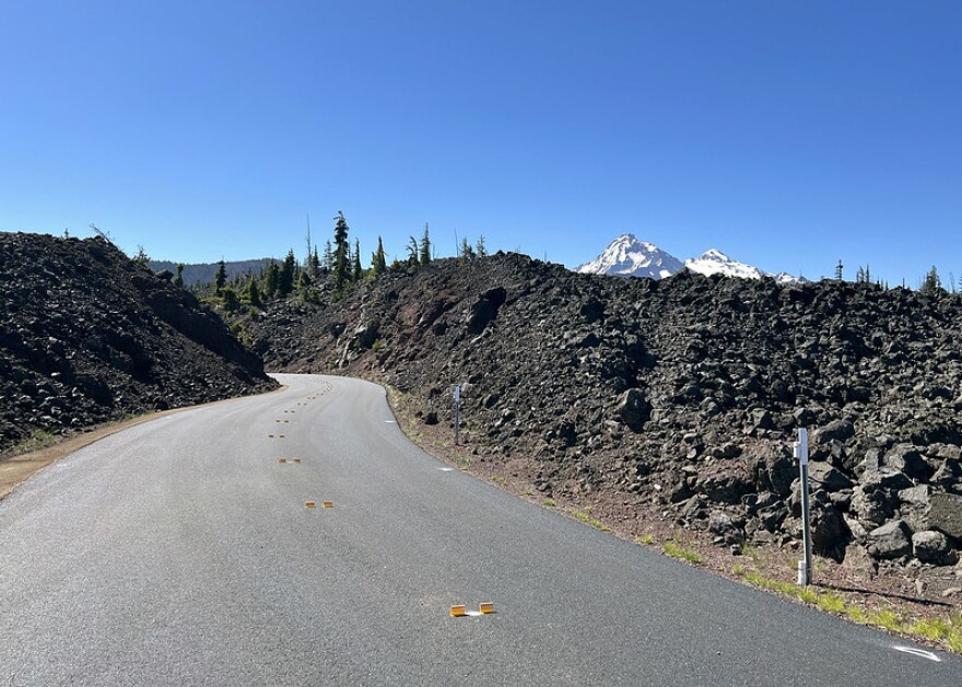 Newly paved road through lava beds with snowcapped mountains in the background.