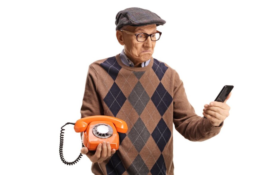 Elderly man holding an old vintage rotary phone and a smartphone.