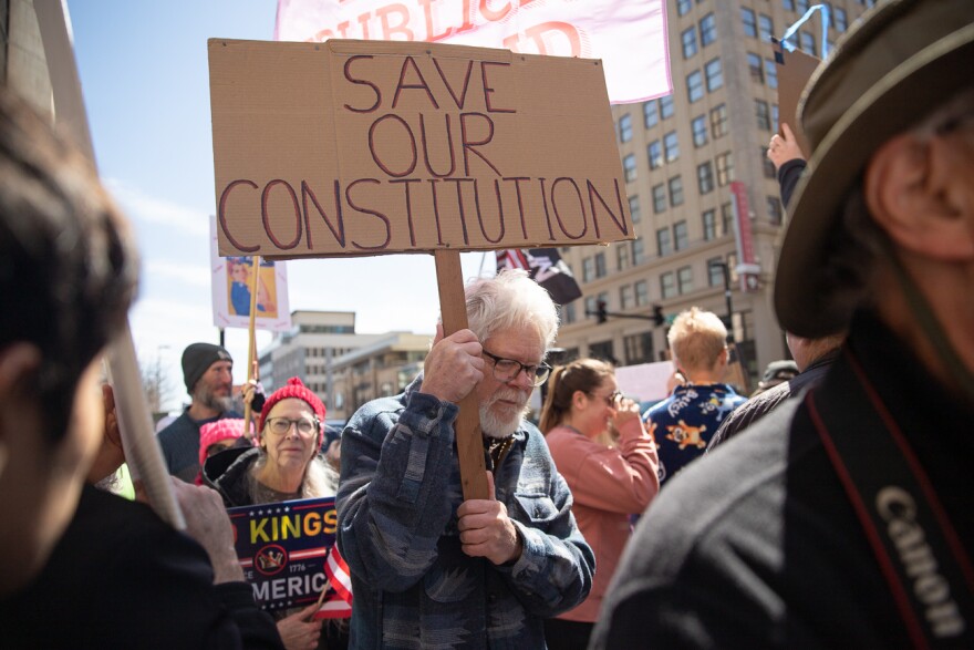 A demonstrator holds a sign reading "Save our Constitution" as he walks through a crowd in Wichita, Kan. on Saturday, March 28, 2026. Demonstrators were escorted and by police throughout the protest.