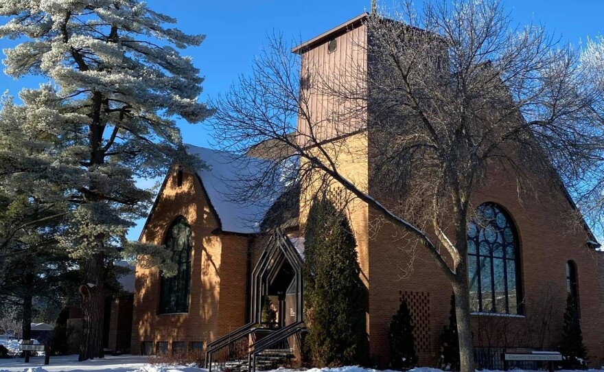 A stately brick church building in the winter with frost on surrounding pine trees against a bright blue sky.