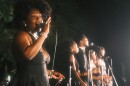 A woman sings on stage with other female backup singers