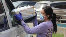 An Oklahoma City Public Schools employee wears a mask while handing food through a car window as part of the district's meal program.