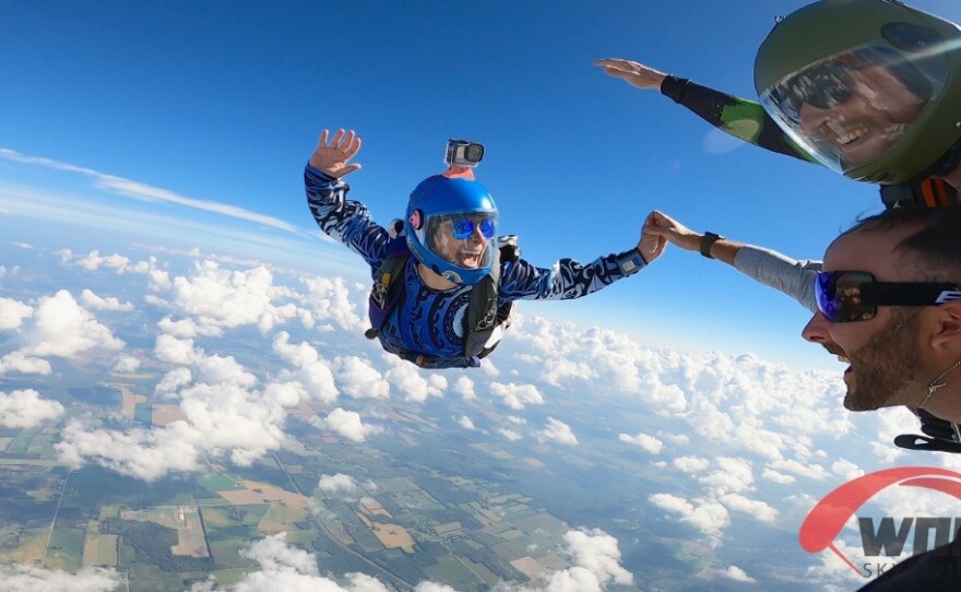 Two skydivers hold hands while floating in the air.
