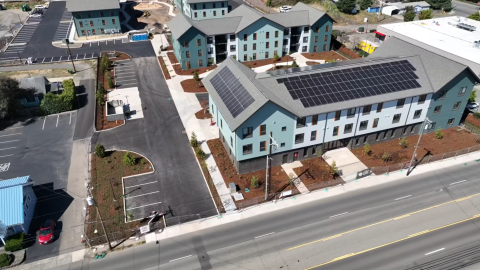 Multiple multistory blue and white buildings are shown on a large lot, with solar panels on the roofs. 