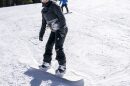 A woman stands on a snowboard on a mountain slope.