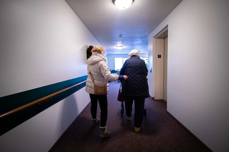 a home healthcare worker helps an elderly woman walk down a hallway